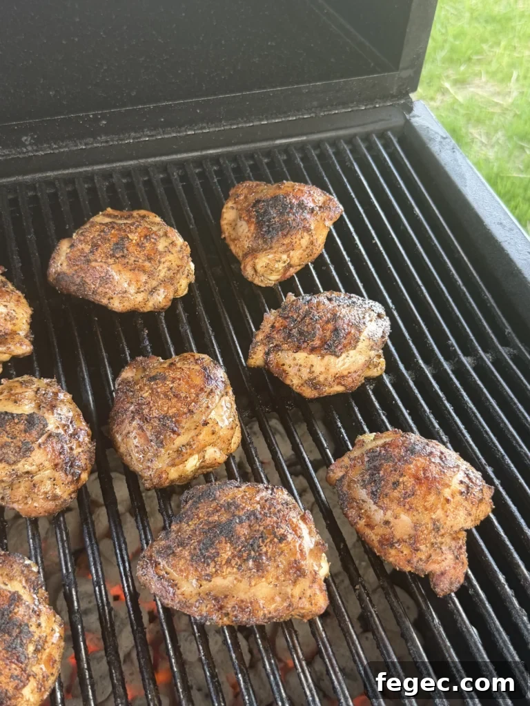 Juicy Grilled Chicken Thighs with Crispy Skin and Garlic Herb Rub 3 Seasoned honey chili crisp chicken thighs cooking on a black grill grate with charred golden-brown skin