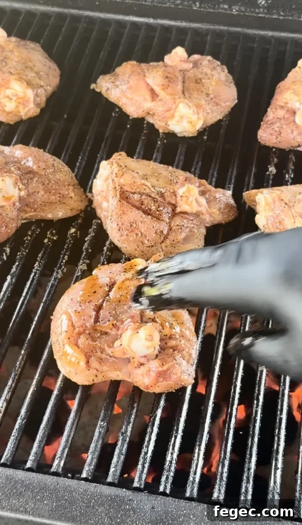 Juicy Grilled Chicken Thighs with Crispy Skin and Garlic Herb Rub 5 Honey chili crisp chicken thighs cooking on grill grates with tongs flipping one piece, showing golden-brown seasoned skin