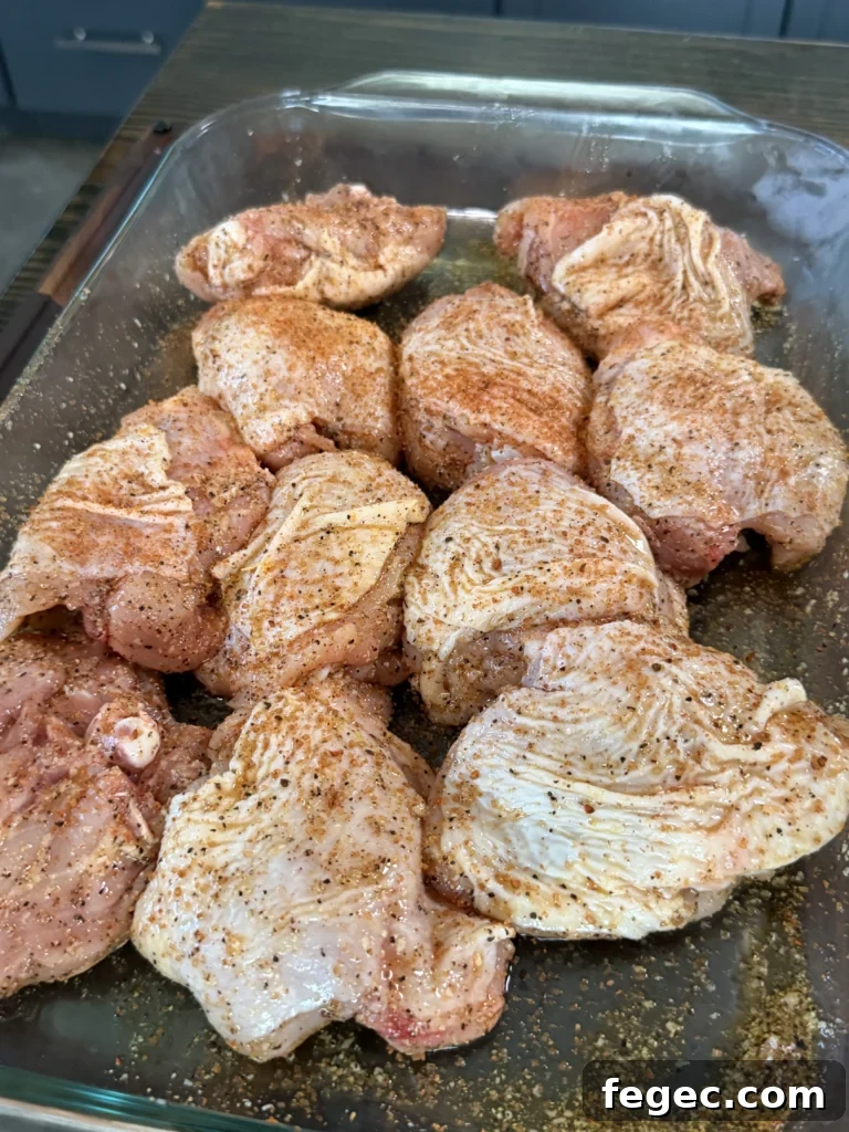 Juicy Grilled Chicken Thighs with Crispy Skin and Garlic Herb Rub 6 Raw chicken thighs seasoned with spices in a clear glass baking dish, ready for honey chili crisp preparation