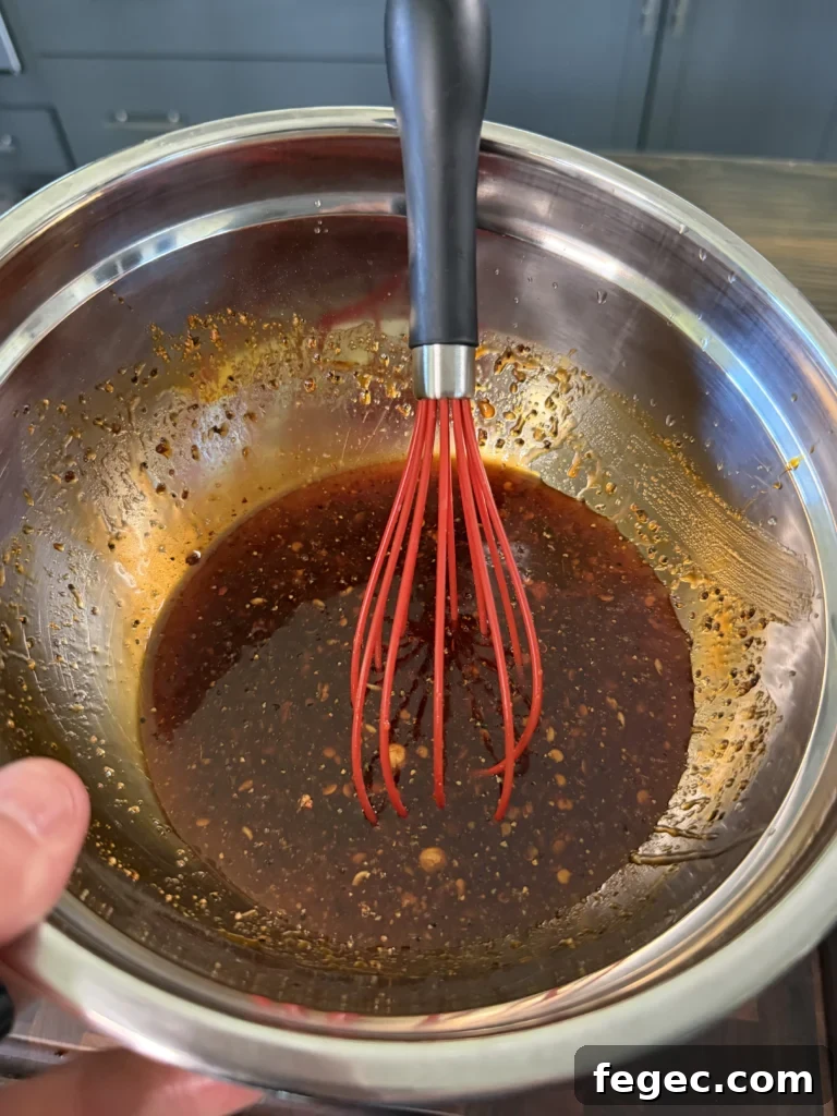 Juicy Grilled Chicken Thighs with Crispy Skin and Garlic Herb Rub 7 Dark honey chili crisp marinade being whisked in stainless steel bowl with red silicone whisk