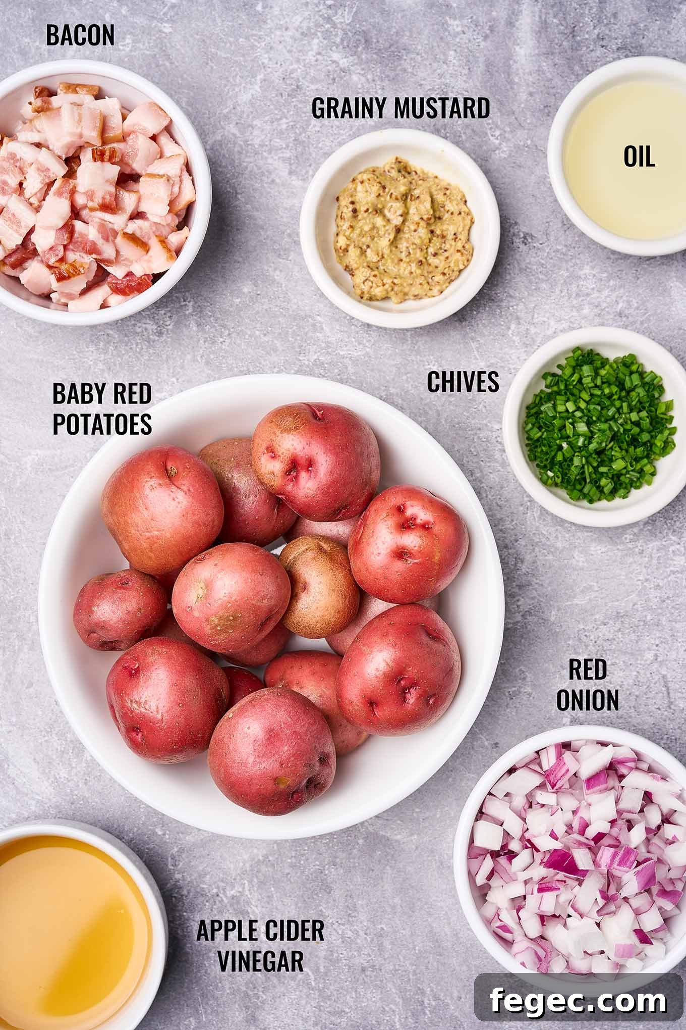 Authentic German Potato Salad with Crispy Bacon and Vinegar Dressing 3 A labeled, overhead view of the ingredients need to make German potato salad including baby red potatoes, red onion, vinegar, chives, bacon, and mustard.