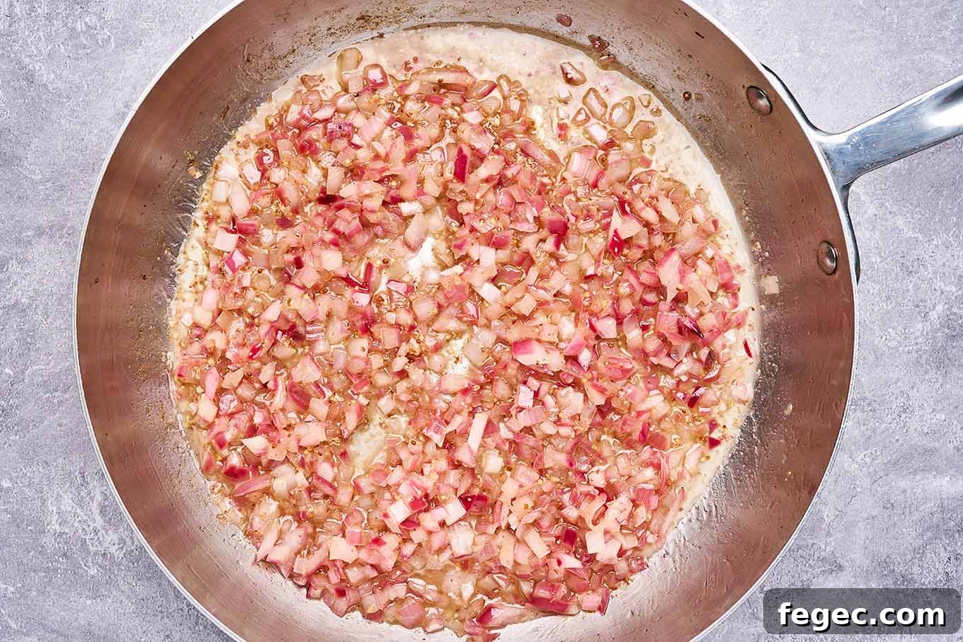 Authentic German Potato Salad with Crispy Bacon and Vinegar Dressing 4 Preparation step for warm bacon dressing featuring an overhead view of a stainless frying pan with diced red onion sautéed in oil and bacon drippings.