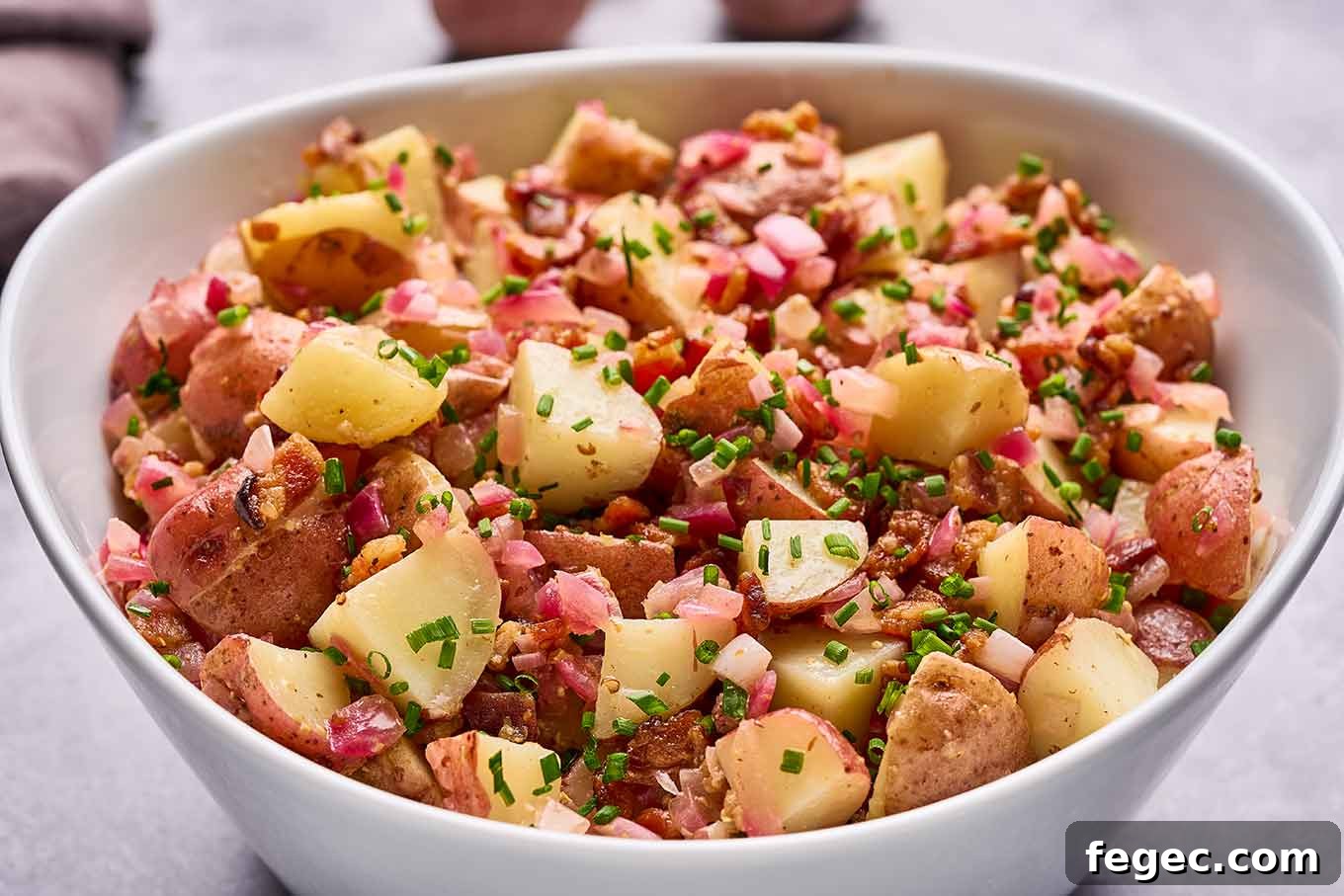 Authentic German Potato Salad with Crispy Bacon and Vinegar Dressing 5 A bowl of German potato salad made with chunks of baby red-skinned potatoes, bacon bits, red onion, chives, and warm bacon dressing.