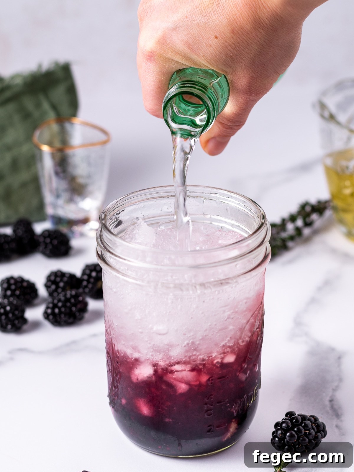 Refreshing Blackberry Smash Mocktail Recipe 7 hand pouring sparkling water into a jar