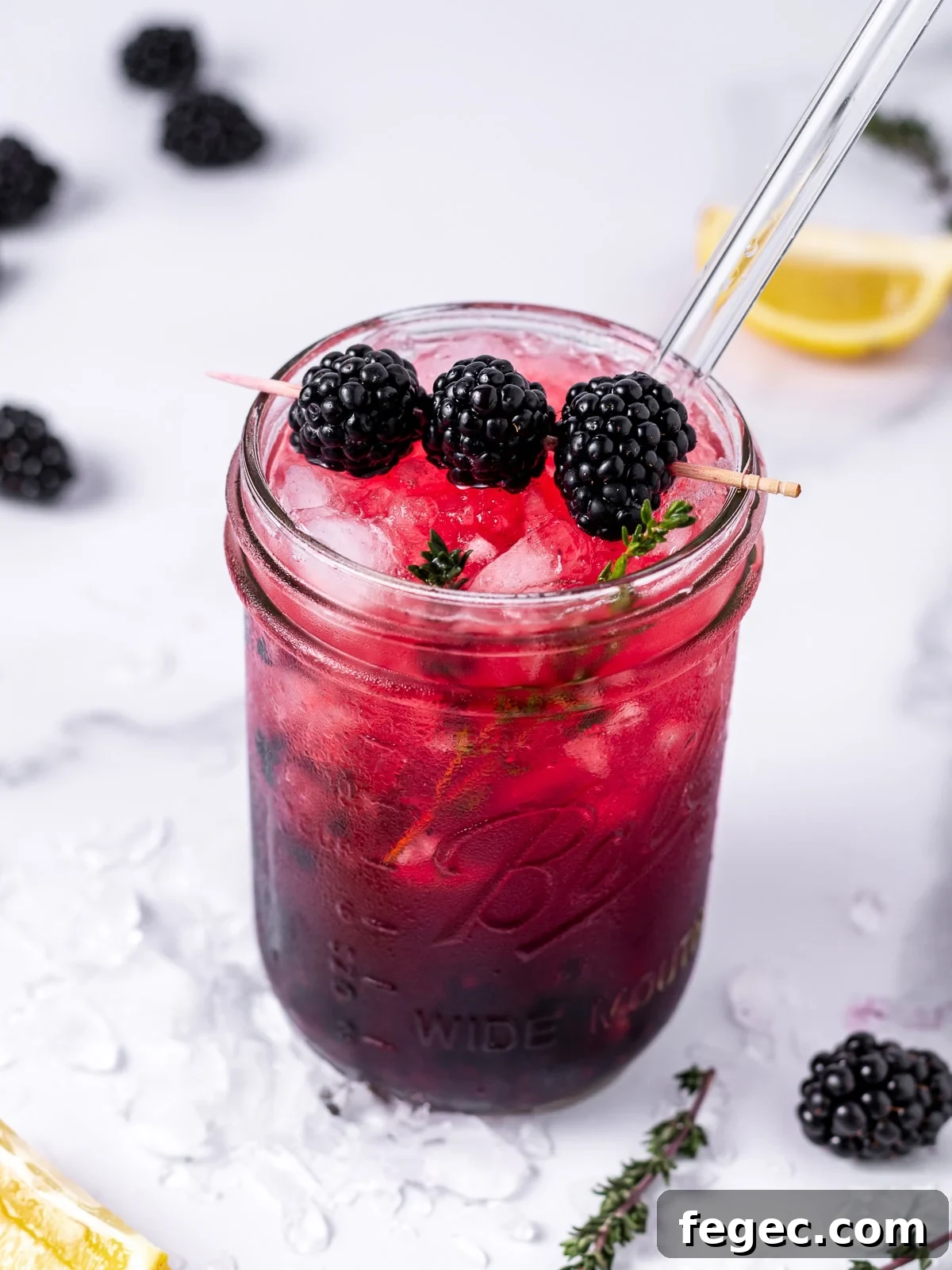 Refreshing Blackberry Smash Mocktail Recipe 9 purple pink blackberry mocktail in a jar with thyme sprigs, lemon wedges, crushed ice and blackberries