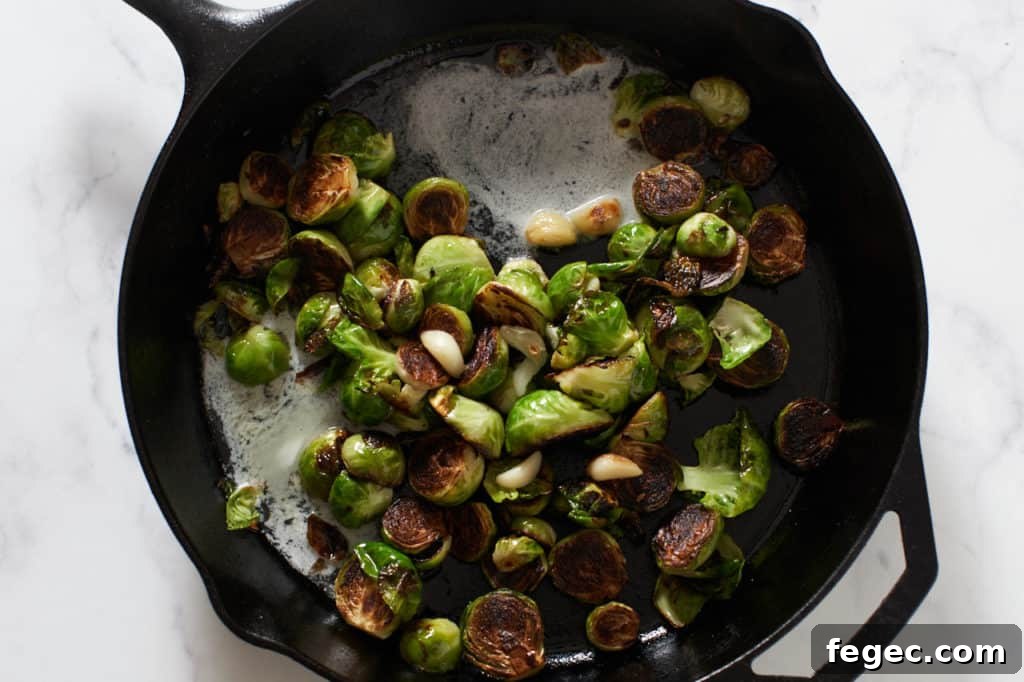 A cast iron skillet with pan fried brussels sprouts being tossed in melting butter to coat them just before serving.