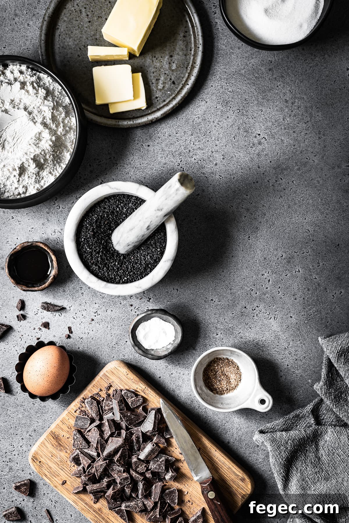 Various bowls and containers filled with ingredients for making cookies arranged on a grey stone background.