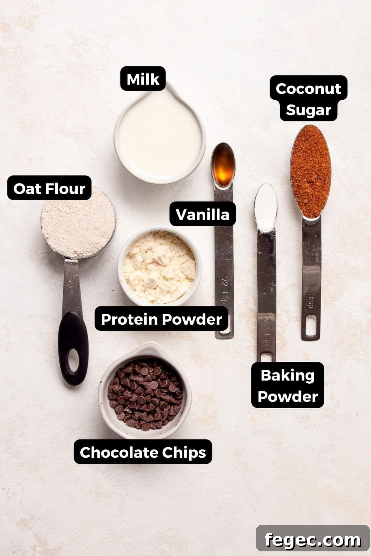Protein Powder Mug Cake Recipe: Quick High-Protein Dessert in Minutes 3 All ingredients in one minute protein mug cake recipe in small bowls including protein powder, oat flour, vanilla extract, coconut sugar, baking powder, milk, and chocolate chips.