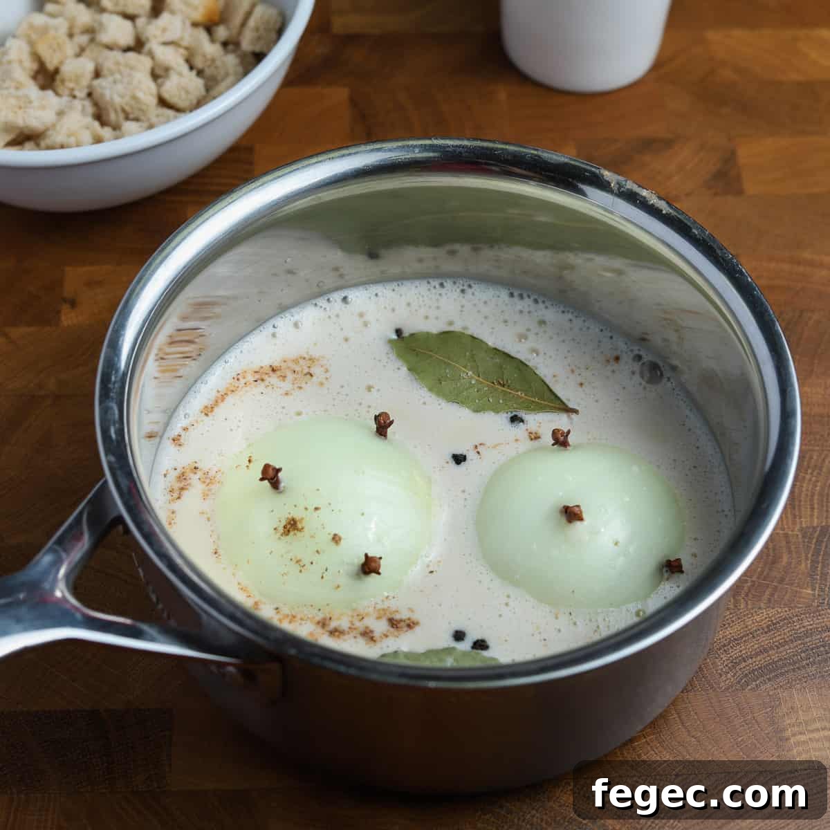Photo of a pan containing oat milk, clove studded onions, bay leaf, and spices.