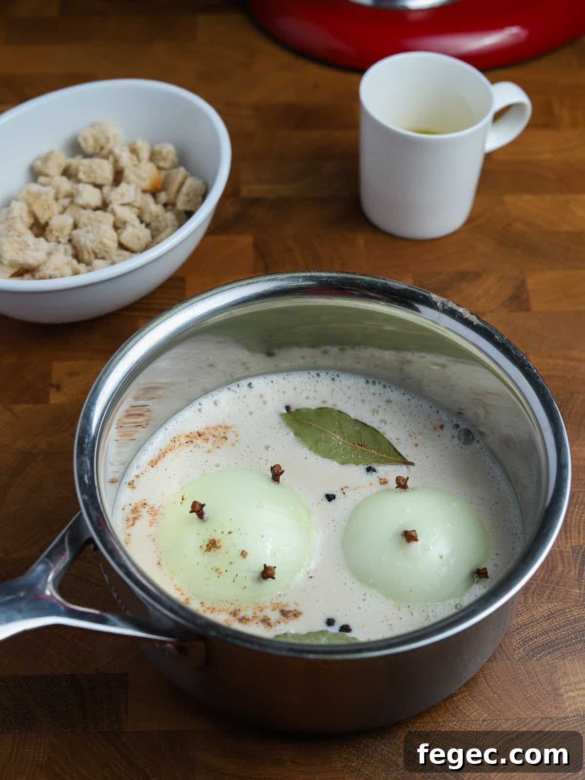 Photo of a pan containing oat milk, clove studded onions, bay leaf, and spices.