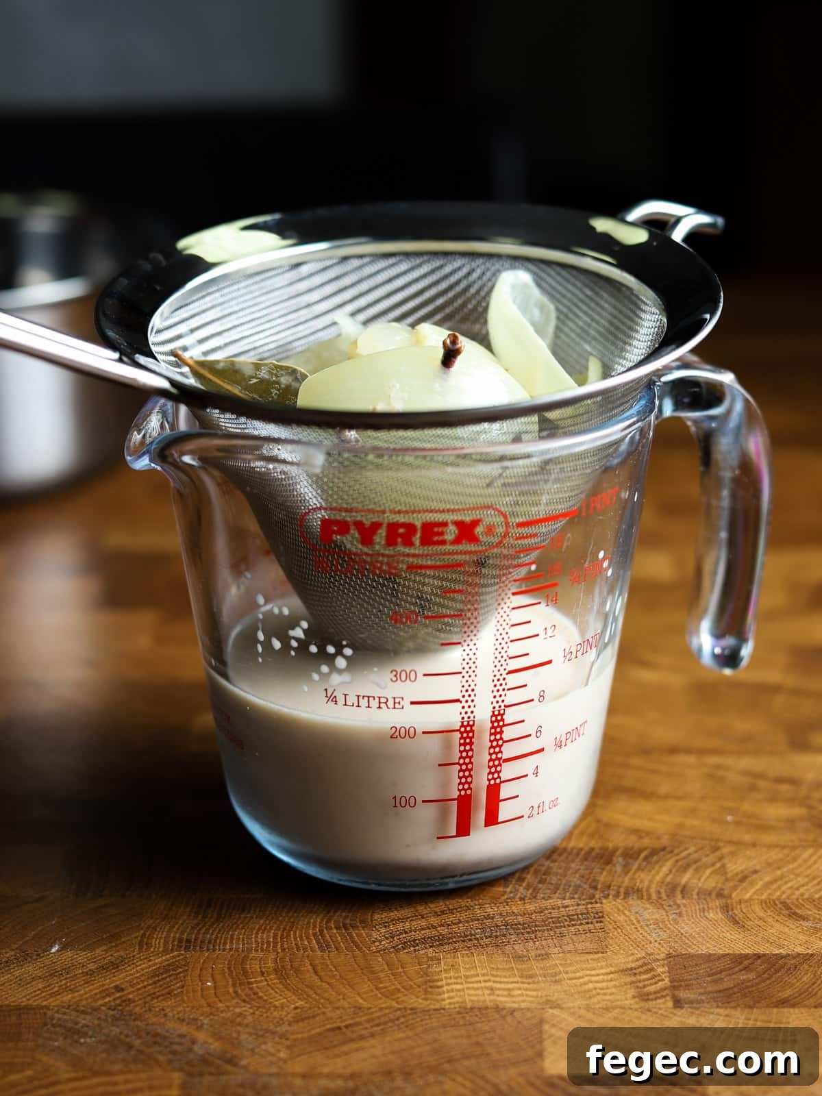 Photo of straining the milk through a sieve over a jug.