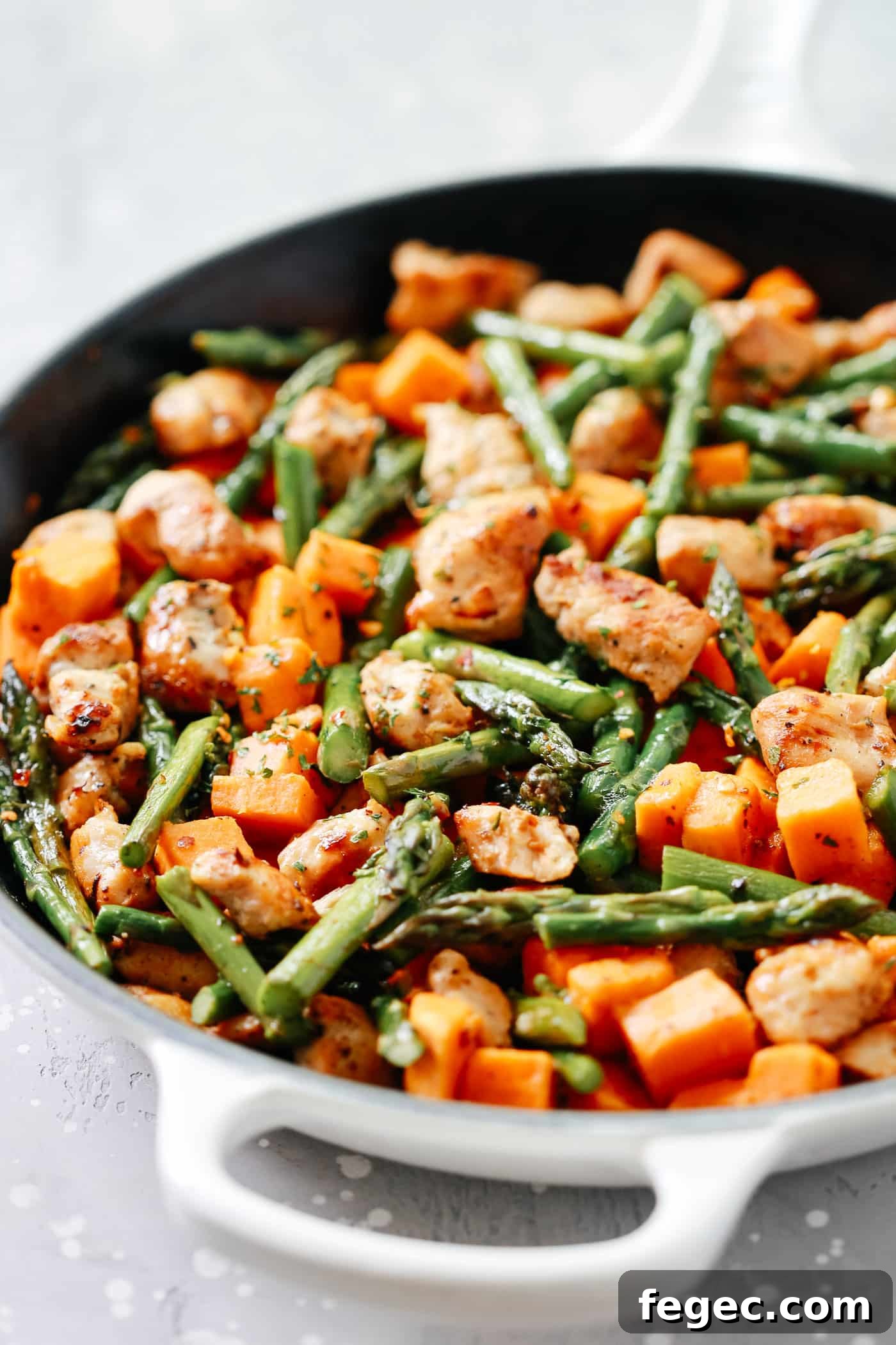 An overhead view of chicken, sweet potatoes, and asparagus in a skillet.