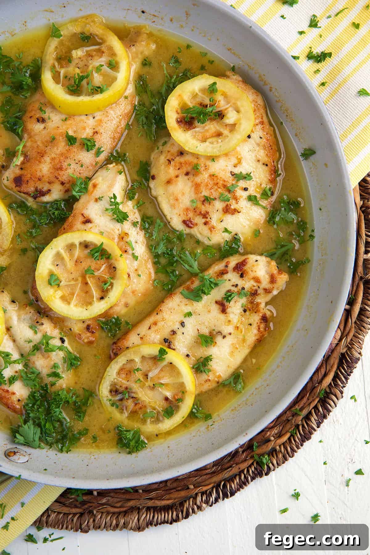 Several chicken breasts with lemons are presented in a skillet.
