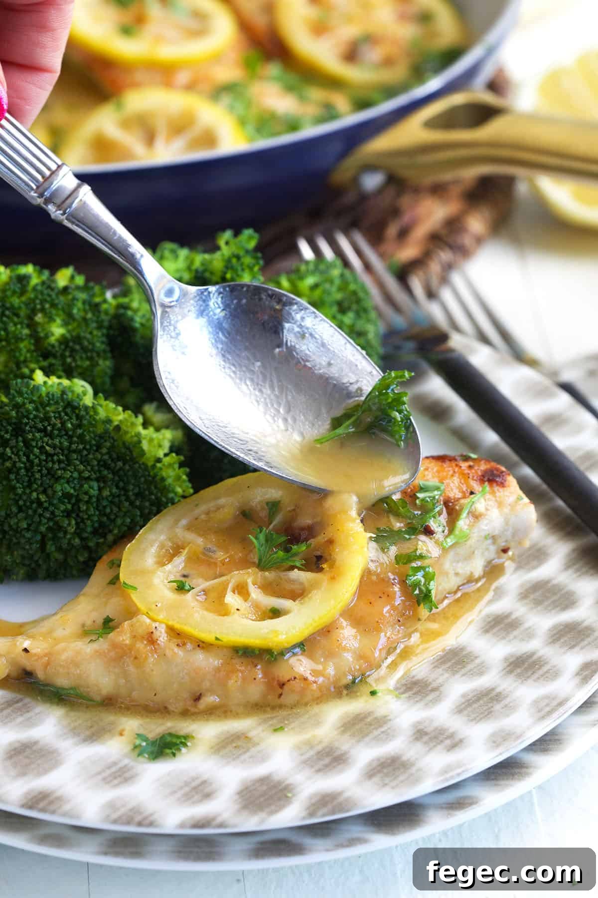 A spoon is drizzling pan sauce on a piece of chicken.