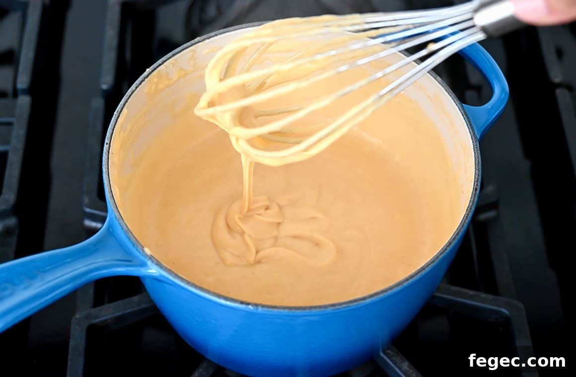 Creamy Beer Cheese Dip Recipe for Game Day Snacks 4 A blue saucepot containing melted cheese with a whisk