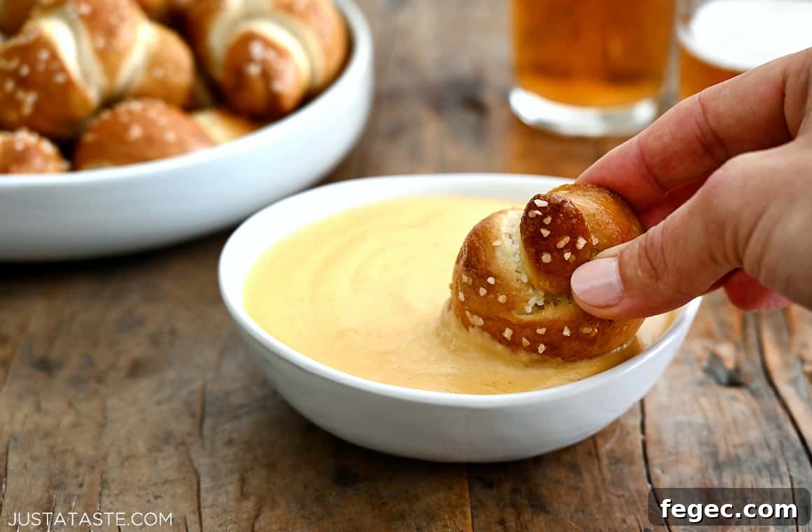 Creamy Beer Cheese Dip Recipe for Game Day Snacks 5 A soft pretzel knot being dunked in a bowl of beer cheese sauce