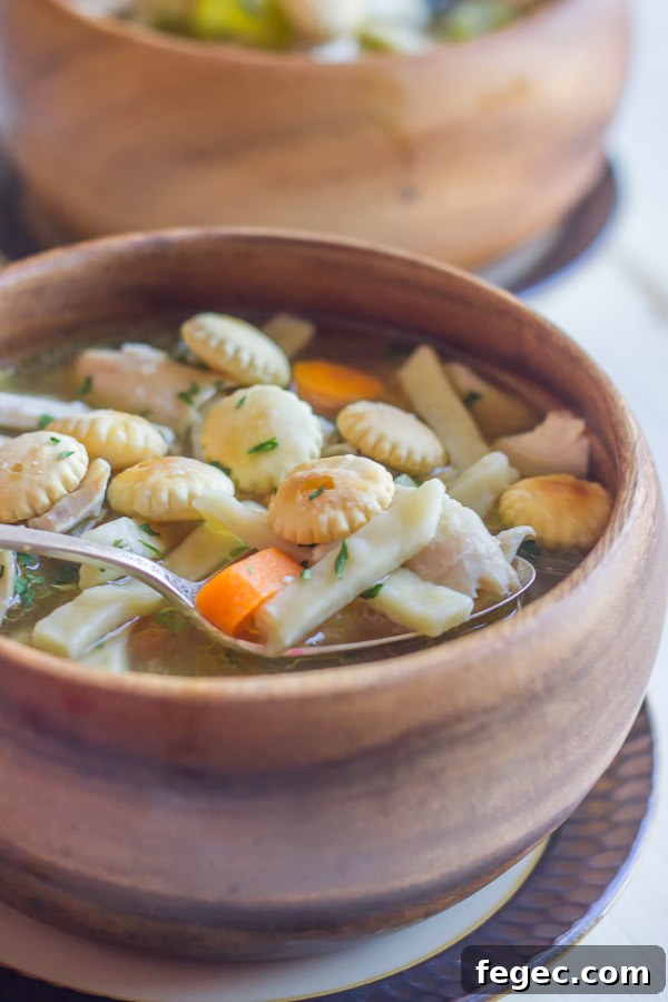 Homemade Chicken Noodle Soup in a bowl with a spoon, topped with oyster crackers.  