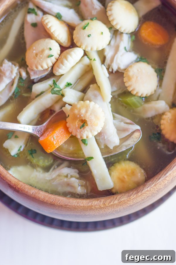 Homemade Chicken Noodle Soup in a bowl with a spoon, topped with oyster crackers.  