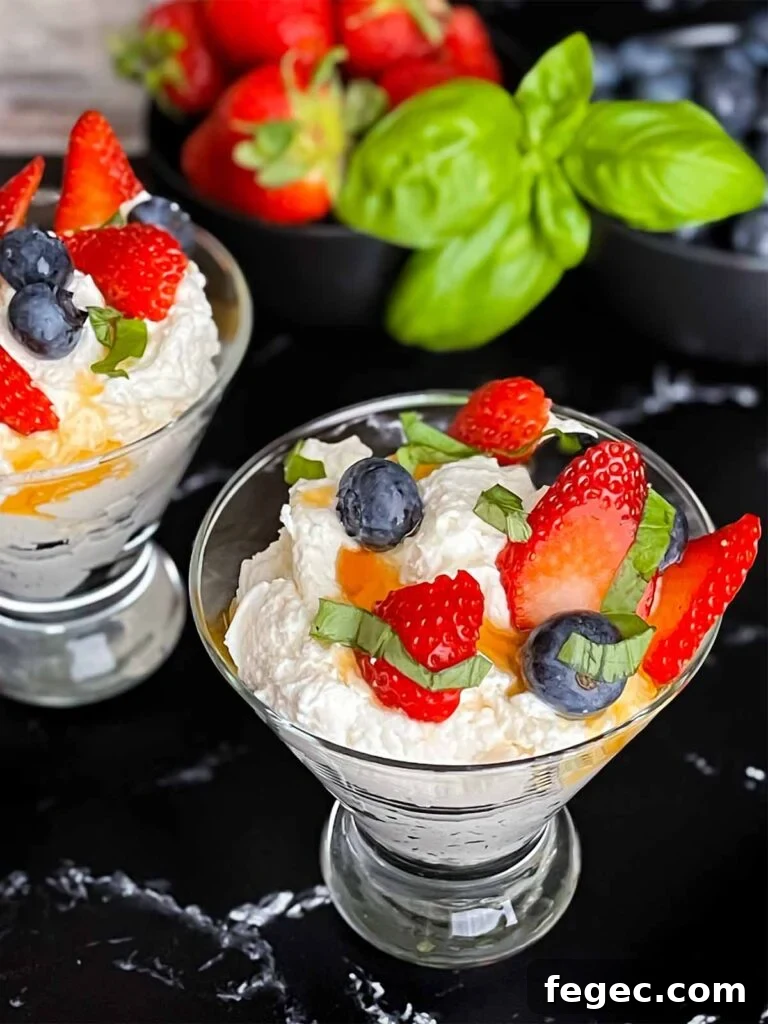 Ricotta mousse in a stemless martini glass garnished with strawberries, blueberries, basil, and honey.