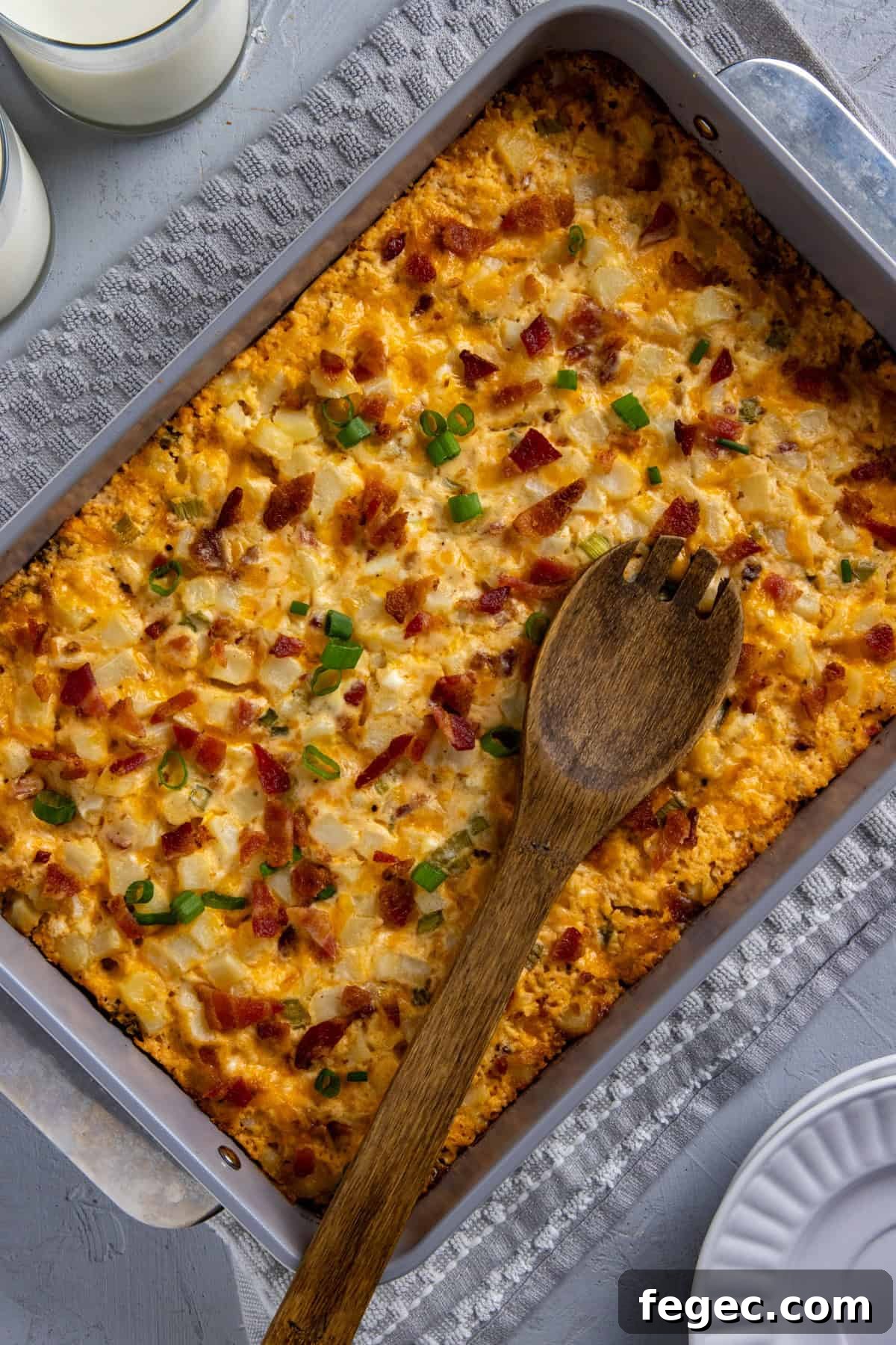 Cheesy Loaded Hash Brown Casserole with Bacon and Green Onions 2 Baked hash brown casserole in stainless steel baking pan with wooden spoon resting on top.
