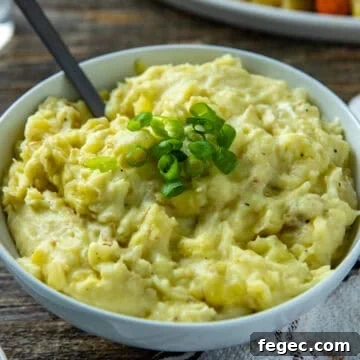 Mashed potatoes in white bowl with sliced green onions as a garnish on top.