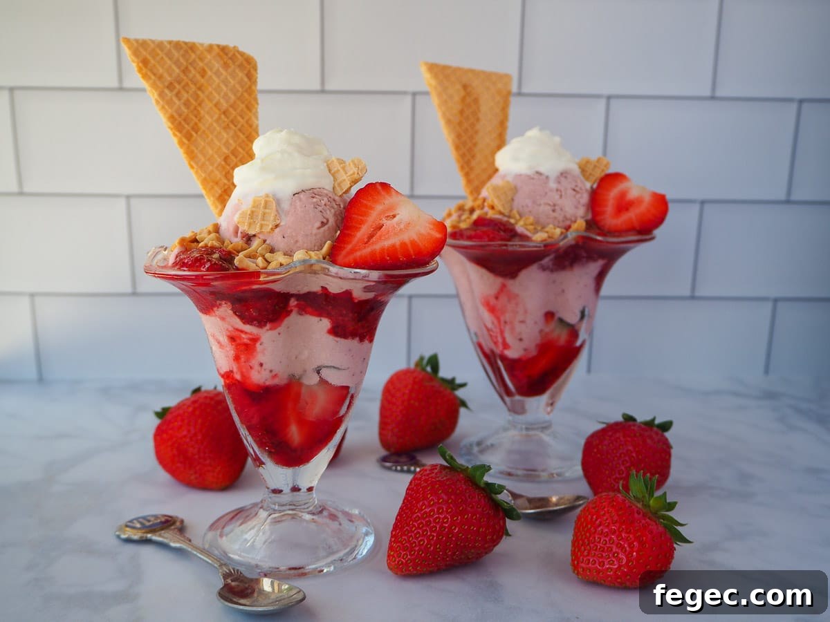 Strawberry sundae with another sundae in the background, surrounded by fresh strawberries and two vintage spoons.
