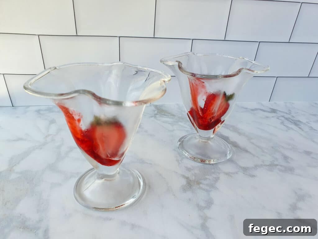 Adding fresh strawberries to the bottom of the sundae glass.