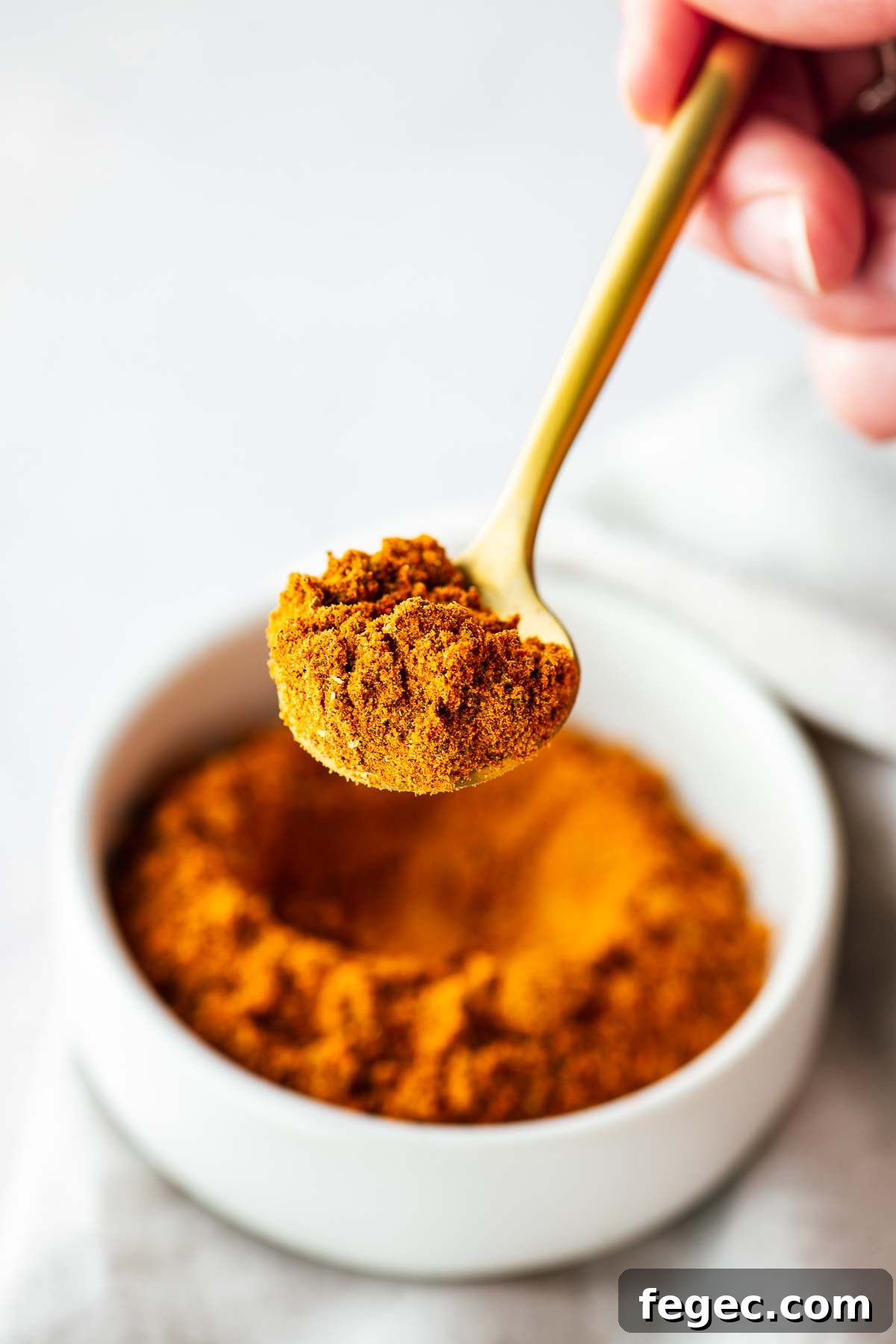 Close-up of homemade Old Bay Seasoning substitute on a gold teaspoon with a bowl of Old Bay in the background.