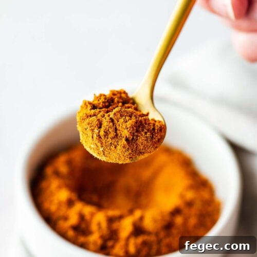 Close-up of homemade Old Bay Seasoning substitute on a gold teaspoon with a bowl of Old Bay in the background.