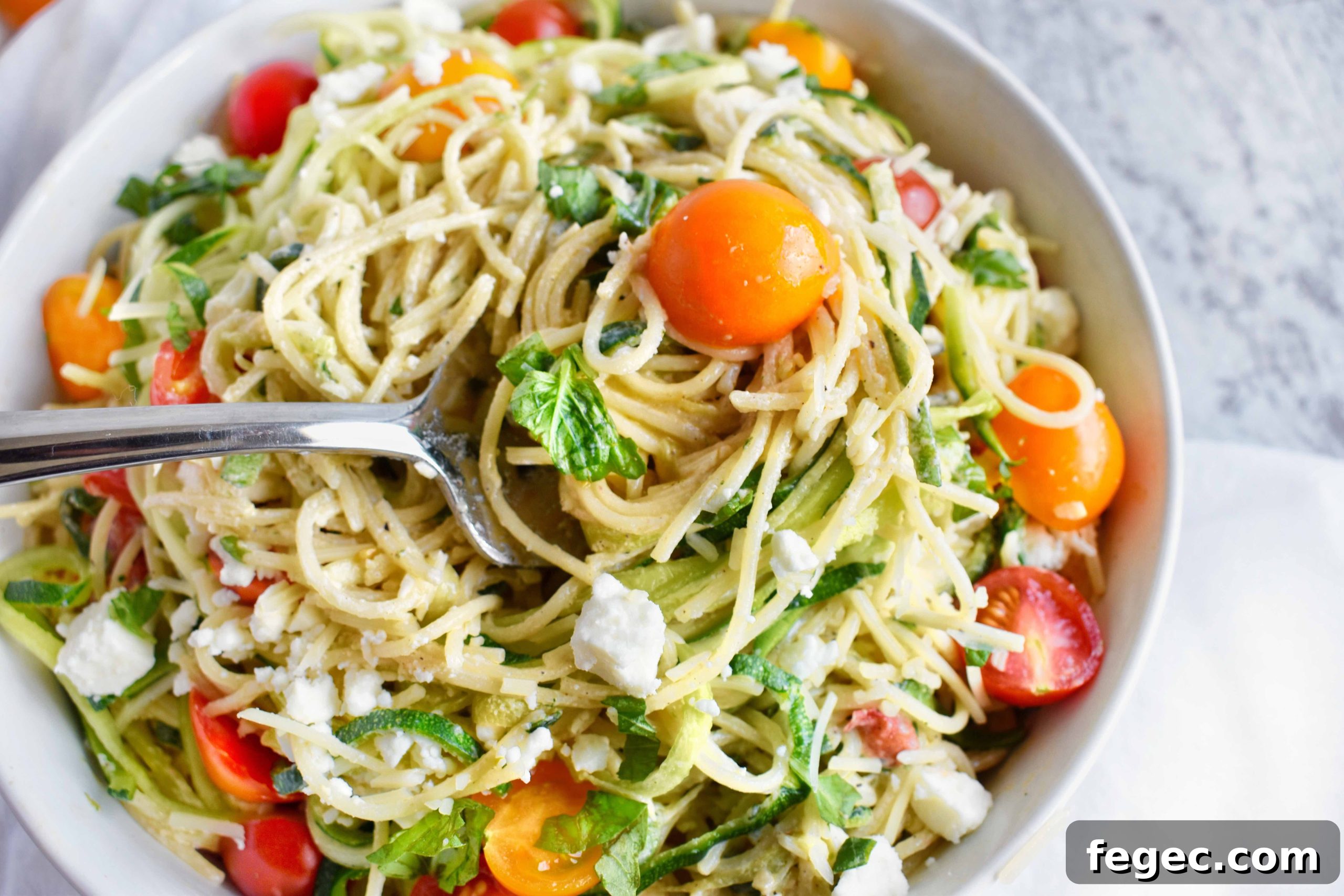 close up of zucchini noodle pasta with creamy yogurt sauce topped with fresh herbs and cherry tomatoes