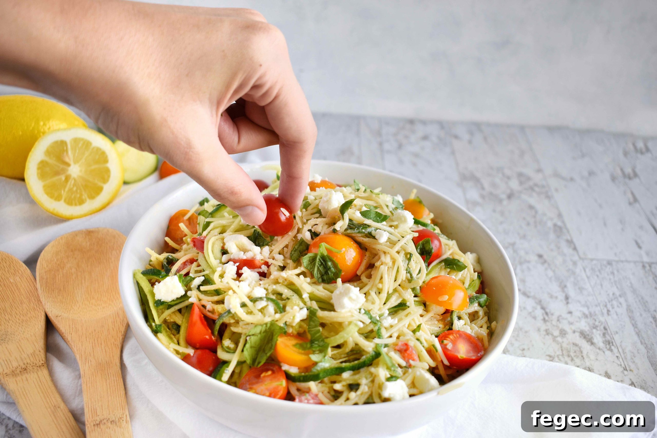 hand picking cherry tomato off of bowl full of zucchini noodle pasta topped with creamy yogurt herb sauce