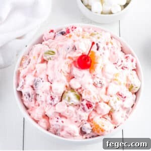 A white bowl on the table filled with fruit salad with Cool Whip.