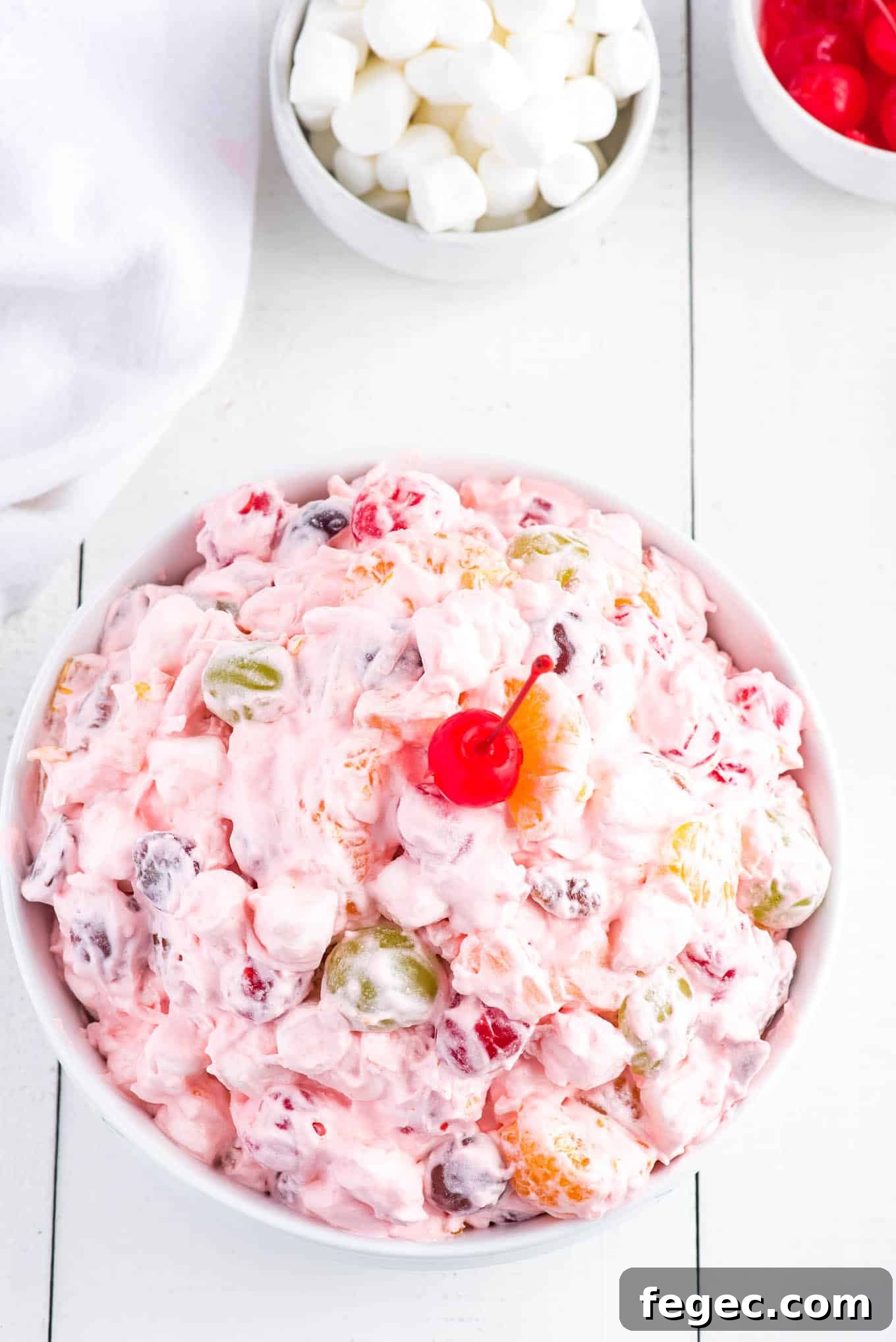 Fruit salad with Cool Whip in a bowl garnished with a maraschino cherry.