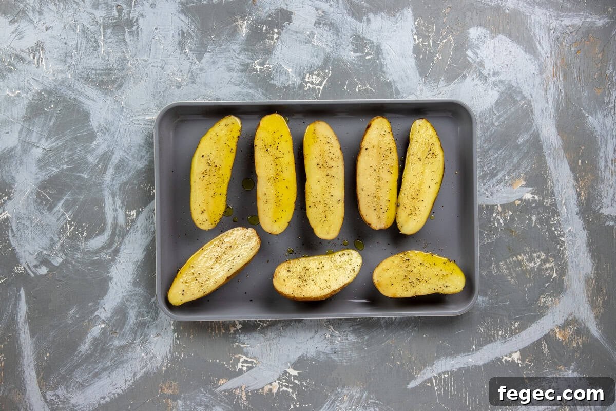 Eight raw, seasoned potato halves on a sheet pan.