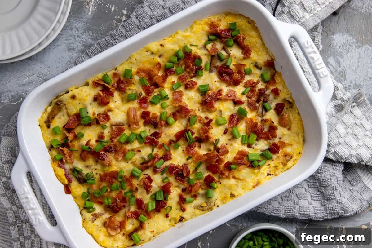 White casserole dish filled with baked mashed potatoes. Garnished with cooked crumbled bacon and sliced green onions.