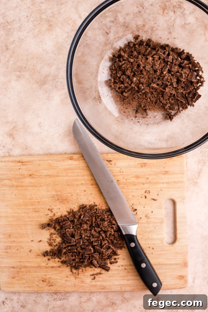 Chopped chocolate on a cutting board and a knife and a bowl of chocolate.