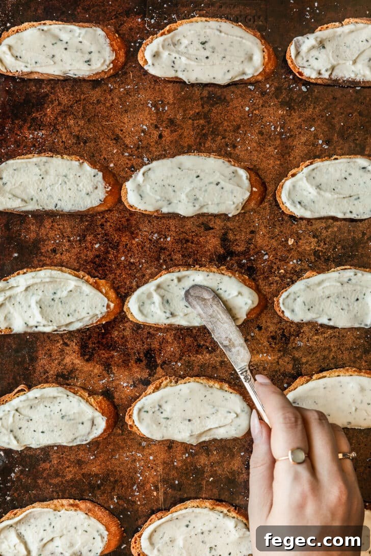 Fig & Goat Cheese Crostini with Honey Drizzle 7 A hand using a knife to spread cheese on toasts.