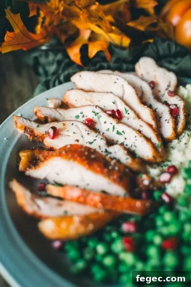 Sliced roasted turkey with garnish of herbs and pomegranate seeds.