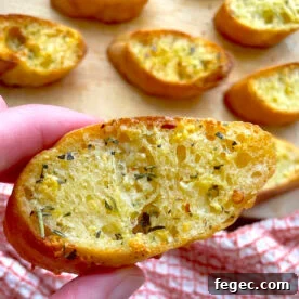 A hand holding buttered garlic toast over several slices on a wooden board.