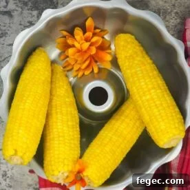 four cooked ears of corn in a silver bowl with orange flowers
