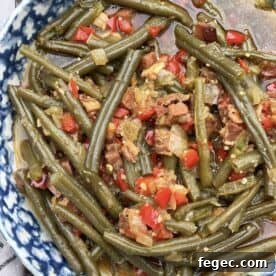 A bowl of southern style green beans cooked in a crock pot with ham, bacon, and red bell peppers.