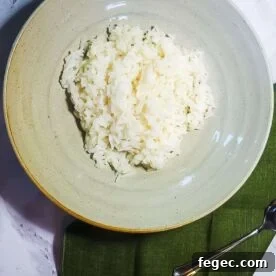 A bowl of white rice on a marble background with a green napkin and a spoon.