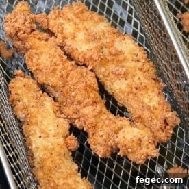 Golden-brown fried chicken tenders resting in a wire basket, showcasing their crunchy coating.