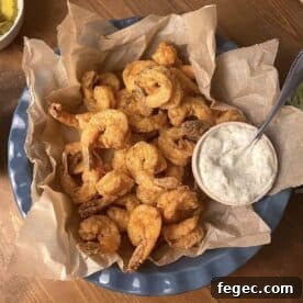 A blue basket of crispy fried shimp with a small bowl of tartar sauce.
