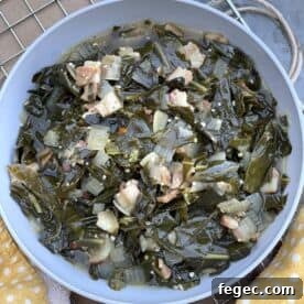 A bowl of southern collard greens on a metal rack with a yellow towel.