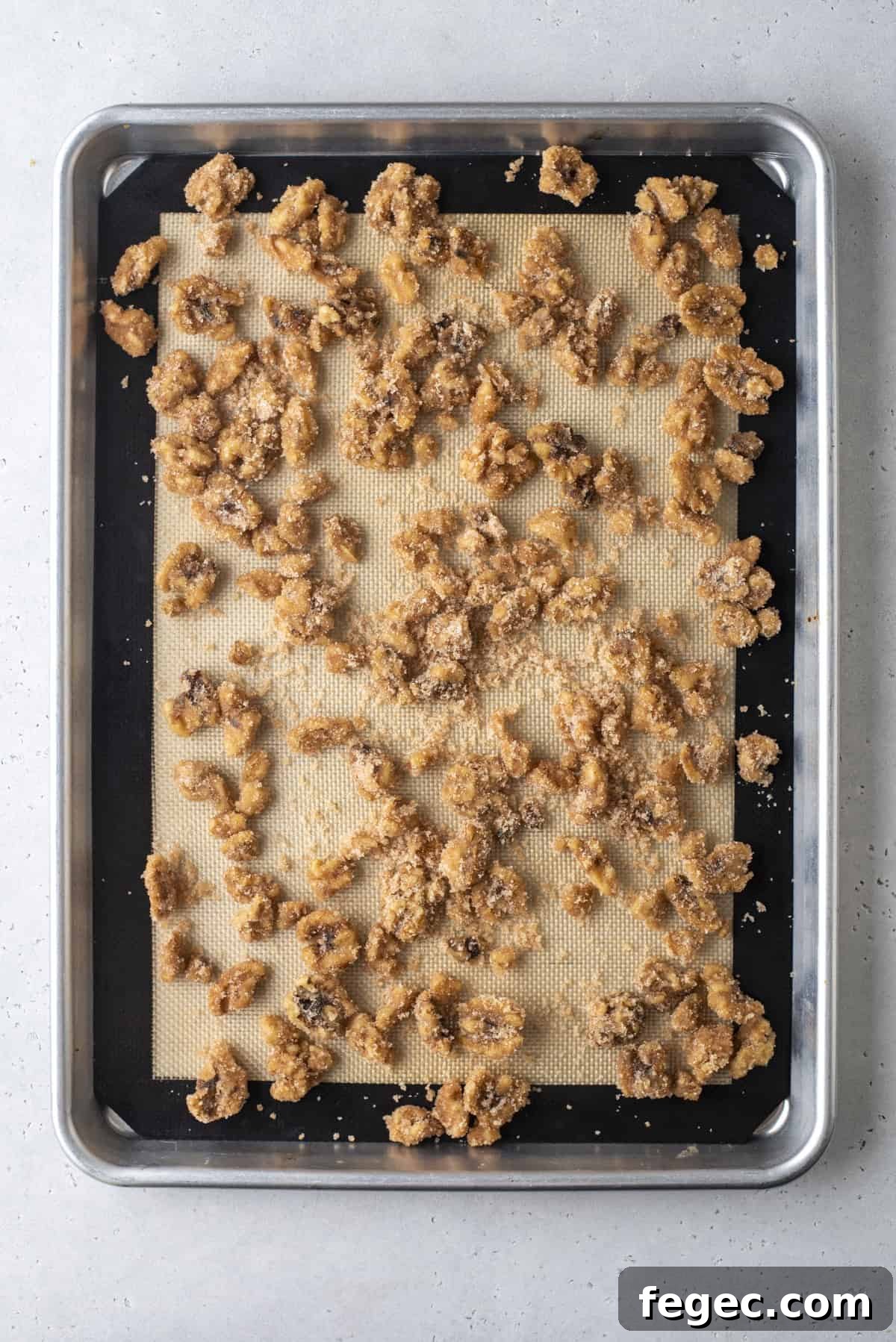 candied walnuts spread onto a baking sheet lined with a silicone baking mat