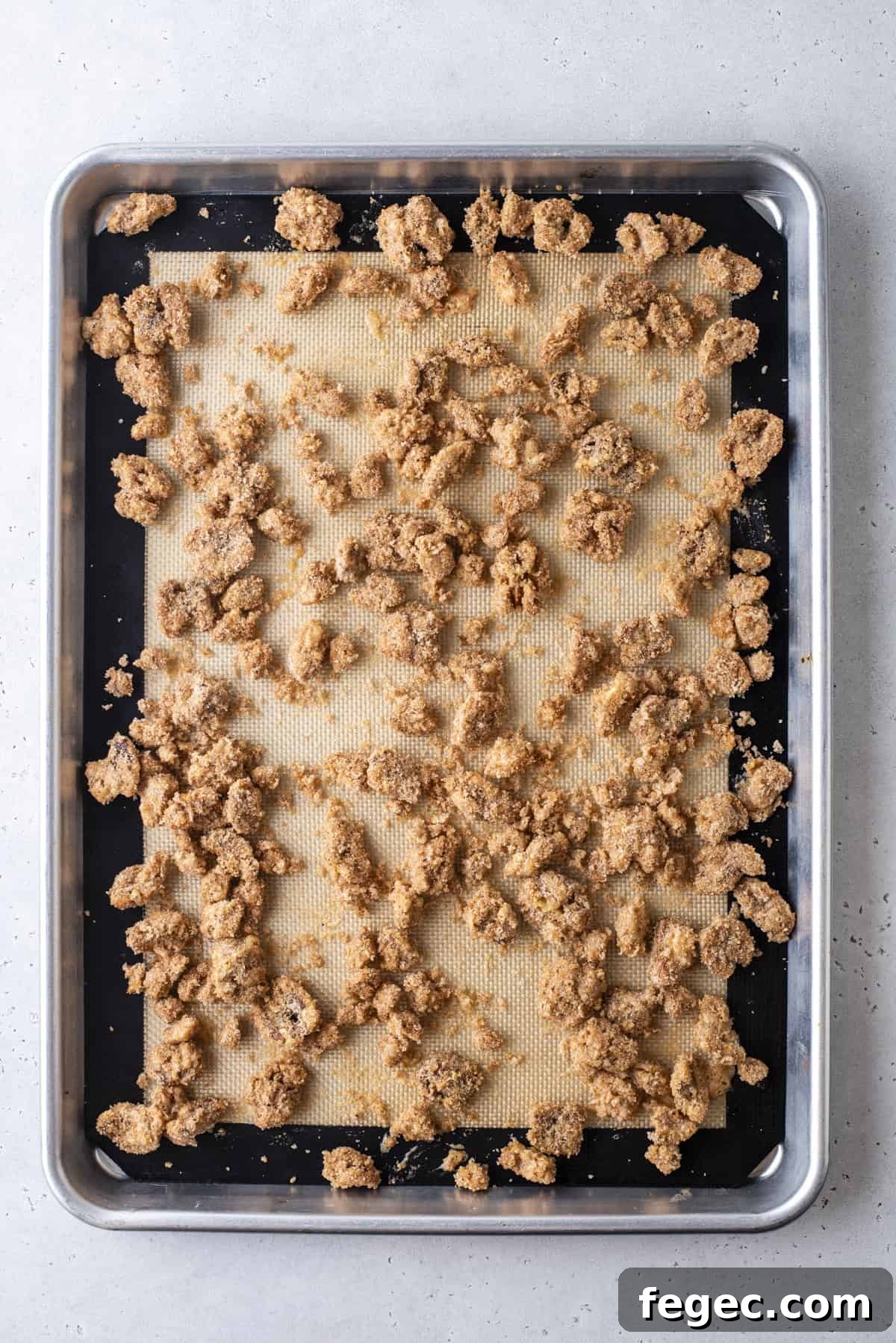 candied walnuts spread onto a baking sheet lined with a silicone baking mat