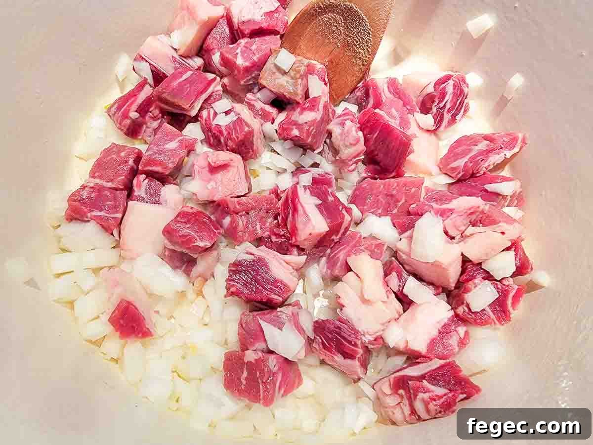 ribeye steak and diced onions cooking in a dutch oven.