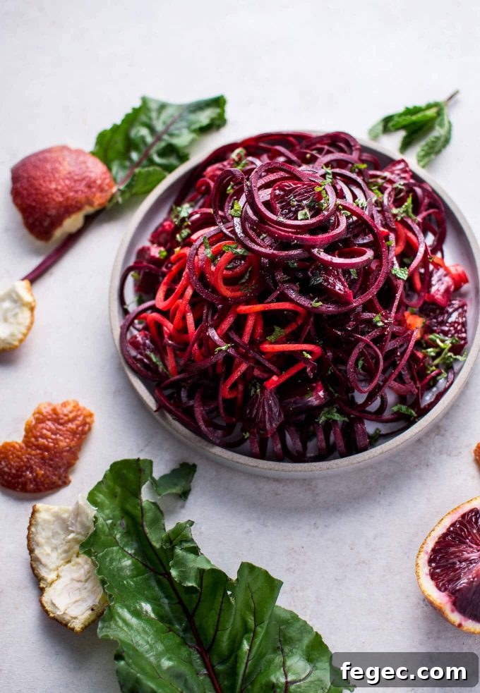 bowl of raw beet and blood orange vegan salad beside orange peels and beet leaves