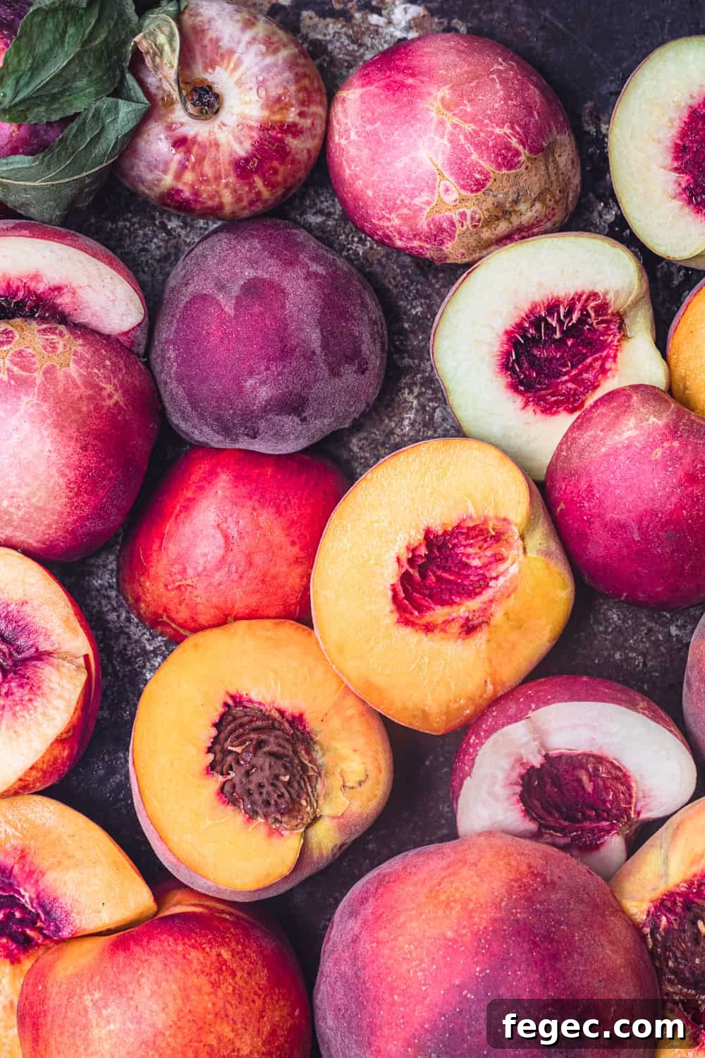 Different varieties of fresh raw peaches, some are cut in half, overhead shot.